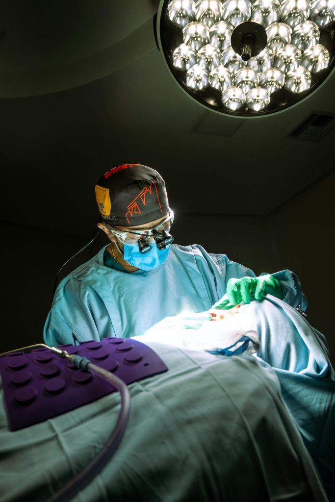 Focused surgeon performing rhinoplasty under bright surgical lights in a sterile operating room.